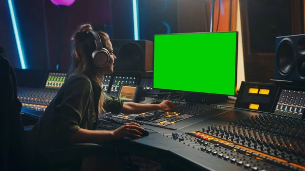 Stylish Female Audio Engineer Producer Working in Music Record Studio, Uses Headphones, Green Screen Computer Display, Mixer Board, Control Desk to Create New Song. Creative Artist Musician.