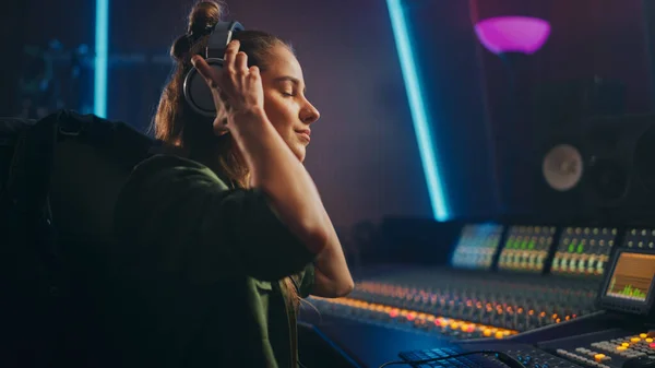 Retrato de una hermosa artista musical femenina en Music Recording Studio poniéndose auriculares. Ella utiliza el tablero de mezcla crear canción moderna. Ingeniera de audio femenina exitosa, productora trabajando . —  Fotos de Stock