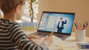 Akıllı çocuk öğretmeniyle video görüşmesi için dizüstü bilgisayar kullanıyor. Ekranda Sınıftan Konuyu Açıklayan Öğretmenle Çevrimiçi Ders Gösteriliyor. E-Eğitim Mesafesi Öğrenme, Evde Eğitim. Omuz üstünden.