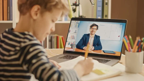 Smart Little Boy verwendet Laptop für Videoanrufe mit seinem Lehrer. Bildschirm zeigt Online-Vorlesung mit Lehrer erklärt Thema aus einem Klassenzimmer, Junge schreibt Informationen nieder. E-Education Fernstudium — Stockfoto