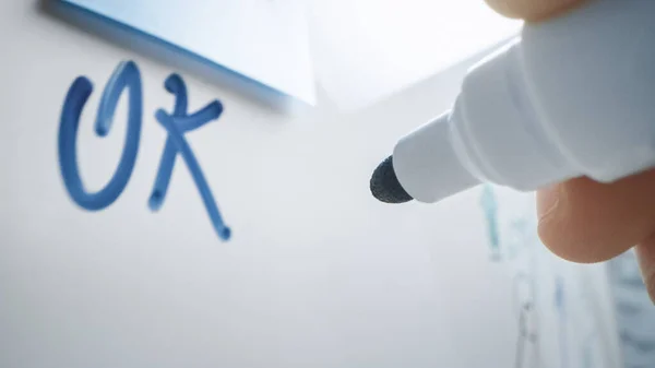 Makroaufnahme eines Blue Marker Pen, der mit einer Hand gehalten wird. Person schrieb "OK" auf Whiteboard mit Grafiken und Businessplänen. — Stockfoto