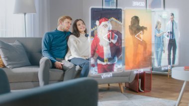 Güzel Genç Çift Evlerinde Bir Koltukta Oturuyor ve Geleceğin Hologram Ekranında İzlenecek Bir Film Seçiyor.