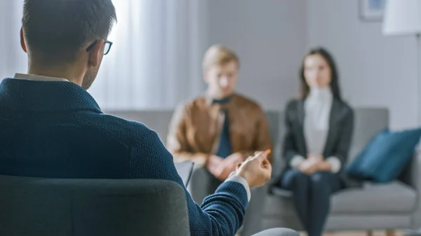 Pareja desenfocada en sesión de consejería con psicoterapeuta. Enfoque en la espalda del terapeuta Tomando notas y hablando: personas sentadas en el sofá del analista, discutiendo problemas psicológicos y de relación —  Fotos de Stock