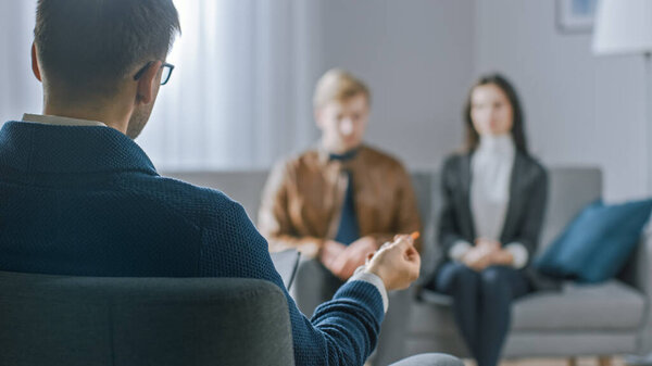 Unfocused Couple on Counseling Session with Psychotherapist. Focus on Back of Therapist Taking Notes and Talking: People Sitting on Analyst Couch, Discussing Psychological and Relationship Problems