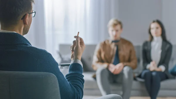 Pareja desenfocada en sesión de consejería con psicoterapeuta. Enfoque en la espalda del terapeuta Tomando notas y hablando: personas sentadas en el sofá del analista, discutiendo problemas psicológicos y de relación — Foto de Stock