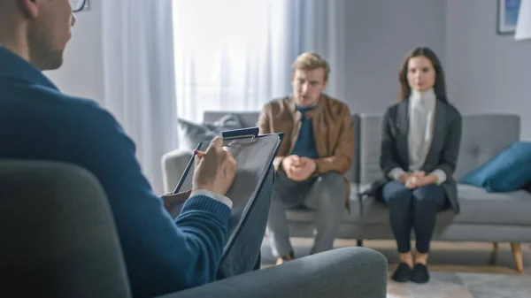 Pareja en una sesión de consejería con un psicoterapeuta. Enfoque de primer plano en la espalda del terapeuta Tomando notas y hablando: personas sentadas en el sofá del analista, discutiendo problemas psicológicos — Foto de Stock