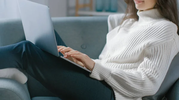 Shot of Young Woman trabalha no computador portátil enquanto está sentado na cadeira. Sensual menina vestindo camisola funciona em estudos de caderno, Surfs Internet, usa as mídias sociais enquanto relaxa no aconchegante apartamento — Fotografia de Stock