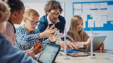 İlköğretim Okulu Sınıfı: Heyecanlı Öğretmenin Tablet Bilgisayarı Tutması Harika Genç Çocuklara Rüzgar Türbinlerinin Nasıl Çalıştığını Açıklıyor. Yenilenebilir Enerjinin Çevre dostu formlarını öğrenen çocuklar