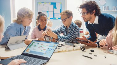 İlköğretim Okulu Robotik Sınıfı: Coşkulu Öğretmen İnşa Etme ve Programlama Robotu olan Çeşitli Zeki Çocuklar Grubu. Yazılım Öğrenen Çocuklar Tasarım ve Yaratıcı Robot Mühendisliği