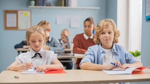 Grundschulklasse: Bunt gemischte Kinder hören aufmerksam zu, wie ihr Lehrer Unterricht gibt Brillante junge Kinder in der Schule schreiben in Schulheften und machen Test. — Stockfoto