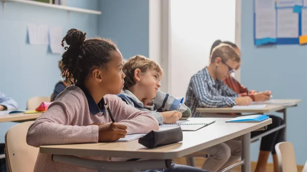 Grundschulklasse: Bunt gemischte Kinder hören aufmerksam zu, wie ihr Lehrer Unterricht gibt Brillante junge Kinder in der Schule lernen, großartige Wissenschaftler, Ärzte, Programmierer und Astronauten zu sein — Stockfoto