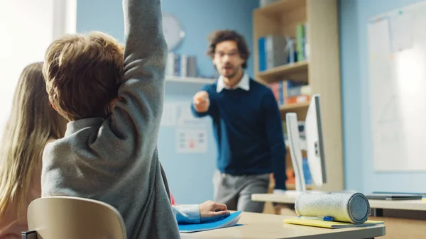 Utalentowany Nauczyciel Wyjaśnia Lekcję Do Klasy Pełnej Jasnych Różnych Dzieci. W szkole podstawowej z grupą inteligentnych dzieci nauka i kreatywne myślenie, chłopiec podnosząc rękę z odpowiedzią — Zdjęcie stockowe