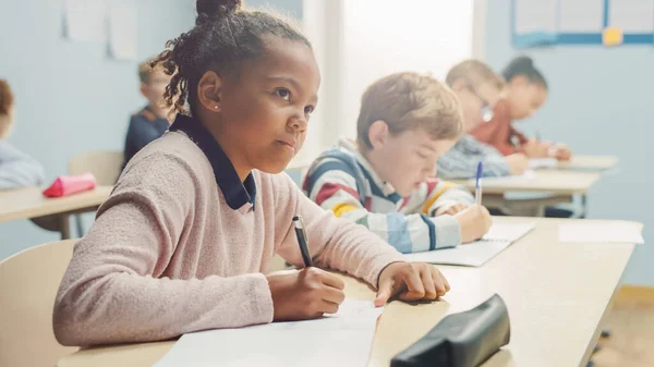 초등 학교 교실에서, 우수 한 흑인 소녀는 시험 과 글쓰기를 위해 운동 연습장에서 글을 쓴다. 다양 한 부류의 어린이들 이 부지런 히 일하고 새로운 것을 배우는 중인 2 학년 교실 — 스톡 사진