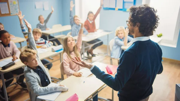 Podstawowa Klasa Różnorodnych Jasnych Dzieci Słuchanie Nauczyciela Udzielającego Lekcji. Każdy podnosi rękę znając prawidłową odpowiedź. Genialne dzieciaki w szkole. Nauczyciel przez ramię Strzał — Zdjęcie stockowe