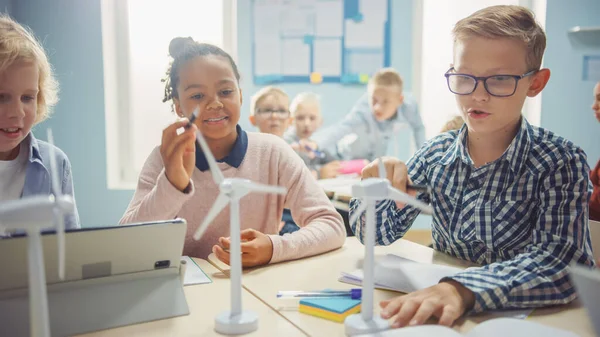 Nella scuola elementare: classe di brillanti bambini piccoli lavorano come un team utilizzando computer tablet per programmare turbine eoliche. Aula con bambini Imparare a conoscere forme ecocompatibili di energia rinnovabile — Foto Stock