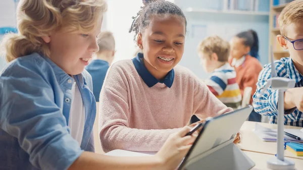 In the Elementary School: Girl and a Boy Work as a Team Using Tablet Computer (en inglés). Aula Diversa con Niños Aprendiendo Lenguaje de Programación y Diseño de Software —  Fotos de Stock