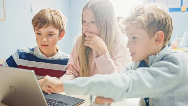 Elementary School Classroom: Diverse Group of Brilliant Children Using Laptop Computer for Software Programming, Talking and Working as a Team (en inglés). Diseño de software de aprendizaje para niños y pensamiento creativo —  Fotos de Stock