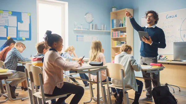 Enthusiastic Teacher Giving a Lesson in Elementary School to Class Full of of Diverse Children. Group of Smart Multiethnic Kids Learning New Stuff. Side View Shot — Stock Photo, Image