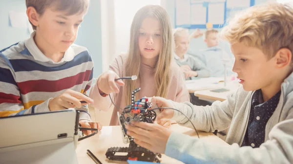 Scuola elementare di robotica in classe: Diversi gruppi di brillanti bambini costruire e programmare robot, parlare e lavorare come un team. Progettazione di software di apprendimento per bambini e ingegneria creativa dei robot — Foto Stock