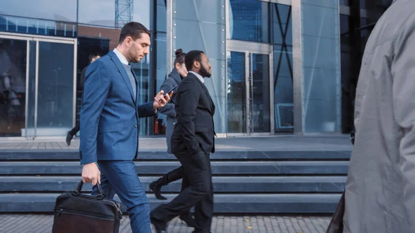 Gerentes de oficina y gente de negocios viajan al trabajo por la mañana o desde la oficina en un día nublado en el centro a pie. Los peatones son inteligentes vestidos casualmente. Personas exitosas sosteniendo teléfonos inteligentes . — Foto de Stock