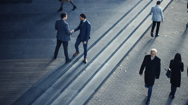 Los gerentes de oficina y los empresarios viajan al trabajo por la mañana o desde la oficina en un día soleado a pie. Los peatones están vestidos con elegancia. Dos hombres de negocios se dan la mano. Disparo desde arriba . — Foto de Stock