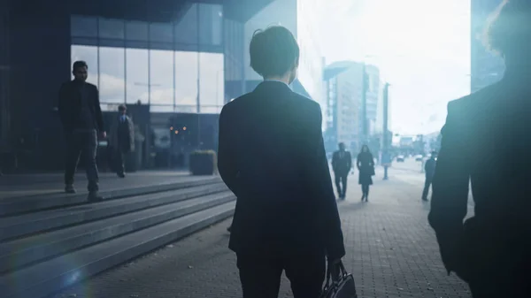Επιχειρηματίας με κοστούμι που περπατάει στο δρόμο. Άλλοι άνθρωποι Γραφείο Μετάβαση στην εργασία ή το σπίτι. Είναι νωρίς το πρωί ή αργά το βράδυ. Πίσω βολή. Αστική Πόλη Φώτα στο παρασκήνιο. — Φωτογραφία Αρχείου
