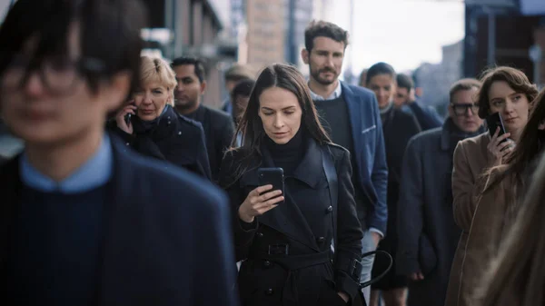 Όμορφη επιχειρηματίας σε μαύρο παλτό χρησιμοποιεί ένα Smartphone σε ένα δρόμο στο κέντρο της πόλης. Περπατάει σε μια πολυσύχναστη οδό πεζών και φαίνεται επιτυχημένη. Περιήγηση στο διαδίκτυο στη συσκευή της. — Φωτογραφία Αρχείου