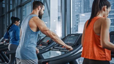 Kaslı Erkek Sporcu, Koşu bandında Koşarken Kablosuz Kulaklık, Podcast ya da Eğitim Çalma Listesi Kullanıyor. Güçlü Sporcular için Bacak ve Kardiyo Spor Günü. Foregorund 'da Koşan Güzel Kadınlar