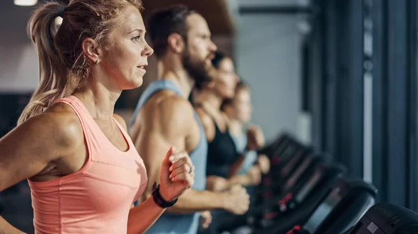 Fit athletische Frau, die auf dem Laufband läuft und ihre Fitnessübungen macht. Muskulöse Frauen und Männer trainieren aktiv in der modernen Turnhalle. Sports People Workout im Fitness Club. Seitenansicht — Stockfoto