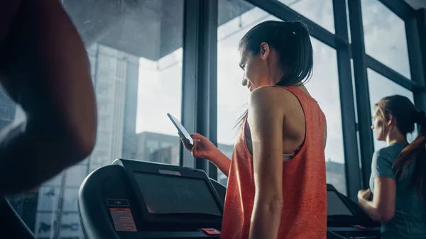 Belle sportive sportive femme dans la salle de gym Courir sur un tapis roulant, utilise Smartphone. Contexte Adapter l'entraînement des athlètes. — Photo