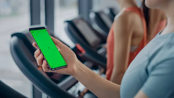 Athletic Woman használja Green Mock-up Screen Smartphone miközben fut a futópad egy edzőteremben. Sport női hozzászólás a közösségi média, veszi képek, órák videók, míg a testmozgás a Fitness Club — Stock Fotó