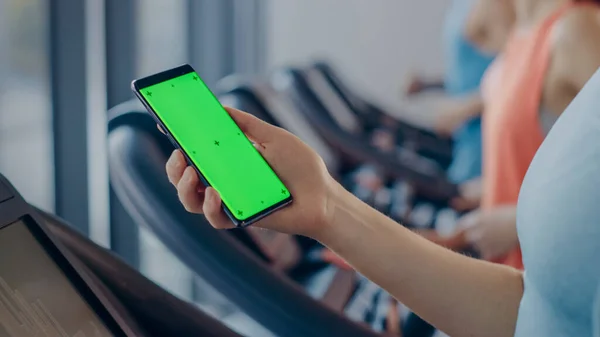 Donna atletica fa gesti durante l'utilizzo di Smartphone schermo verde e in esecuzione sul tapis roulant in una palestra. Fit femminile Messaggi sui social media, Fotografie, Orologi Video, Esercizi nel Fitness Club — Foto Stock