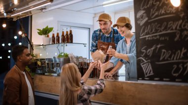 Yemek kamyonu çalışanı Mutlu Genç Hipster Müşterisine Burger Veriyor ve Soğuk İçecek Veriyor. Modern Cool Mahallesi 'nde Sokak Yiyecekleri satan başarılı bir Ticari Kamyon.