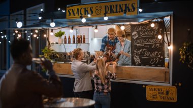 Yemek kamyonu çalışanı Mutlu Genç Hipster Müşterilerine Yeni Yapılmış Biftek Burgerleri, Kızartmalar ve Soğuk İçecekler Veriyor. Modern Havalı Mahallede Sokak Yemeği Satan Ticari Kamyon.
