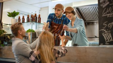 Yemek kamyonu çalışanı Mutlu Genç Hipster Müşterilerine Yeni Yapılmış Biftek Burgerleri, Kızartmalar ve Soğuk İçecekler Veriyor. Modern Havalı Mahallede Sokak Yemeği Satan Ticari Kamyon.