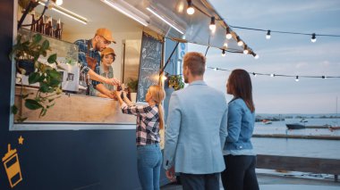 Yemek kamyonu çalışanı hamburger, patates kızartması ve soğuk içecekleri mutlu hippi müşterilere dağıtıyor. İnsanlar dışarıda yemek yiyor. Ticari Kamyon Deniz Kenarı Modern Bir Yer 'de Sokak Yiyeceği Satıyor.