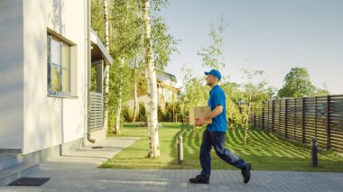 Delivery Man Holding Card Board Package Enters Through the Gates and Walks to the House and Knocks. Delivering Postal Parcel. In the Background Beautiful Suburban Neighbourhood. Side View clipart