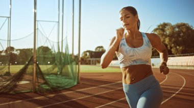 Açık Mavi Atletizm Üstündeki Güzel Spor Kadını ve Stadyumda Koşu Yapıyor. Sıcak bir Yaz Öğleden Sonrası 'nda Hızlı Koşuyor. Sporcu Rutin Spor Uygulaması Yapıyor.
