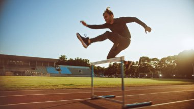 Stadyumdaki sıcak bir yaz akşamında Gri Gömlekli Atletik Formalı Adam ve Atlayan ve Bariyerlerin Üzerinden Atlayan Şortlu. Sporcu Rutin Spor Uygulaması Yapıyor.