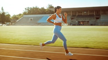 Açık Mavi Atletizm Üstündeki Güzel Spor Kadını ve Bir Stadyumda Koşu Yapıyor. Sıcak bir Yaz Öğleden Sonrası 'nda Hızlı Koşuyor. Sporcu Rutin Spor Uygulaması Yapıyor.