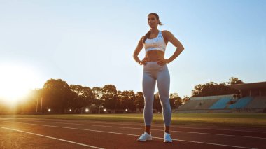 Açık Mavi Atletizm Üstündeki Güzel Spor Kadını ve Leggings Stadyumda Soluklanıyor ve Poz Veriyor. Sıcak bir yaz öğleden sonrasında antrenman yapıyordu ve rutin egzersizini yapıyordu..