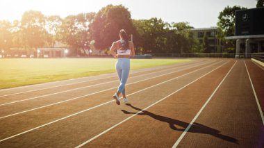 Açık Mavi Atletizm Üstündeki Güzel Spor Kızı ve Stadyumda Koşu Yapıyor. Sıcak bir yaz öğleden sonrasında koşuyor. Sporcu, Rutin Spor Uygulamasını Pistte Yapıyor.