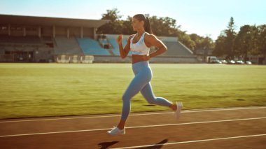 Açık Mavi Atletizm Üstündeki Güzel Spor Kızı ve Stadyumda Koşu Yapıyor. Sıcak bir Yaz Öğleden Sonrası 'nda Hızlı Koşuyor. Sporcu Rutin Spor Uygulaması Yapıyor.