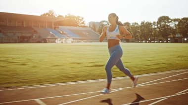 Açık Mavi Atletizm Üstündeki Güzel Spor Kızı ve Stadyumda Koşu Yapıyor. Sıcak bir yaz öğleden sonrasında koşuyor. Sporcu, Rutin Spor Uygulamasını Pistte Yapıyor.