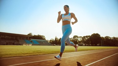 Açık Mavi Atletizm Üstündeki Güzel Spor Kadını ve Bir Stadyumda Koşu Yapıyor. Sıcak bir yaz öğleden sonrasında koşuyor. Sporcu, Rutin Spor Uygulamasını Pistte Yapıyor.