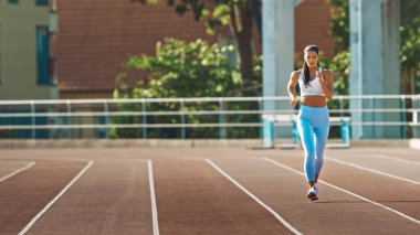 Açık Mavi Atletizm Üstündeki Güzel Spor Kadını ve Bir Stadyumda Koşu Yapıyor. Sıcak bir yaz öğleden sonrasında koşuyor. Sporcu, Rutin Spor Uygulamasını Pistte Yapıyor.