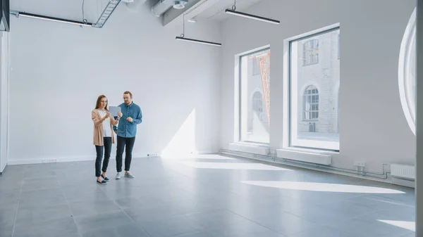 Young Hipster Man and Female Stand in an Empty White Office та Map it with an Augmented Reality Software on a Tablet. Сонячне світло світить через великі вікна. — стокове фото