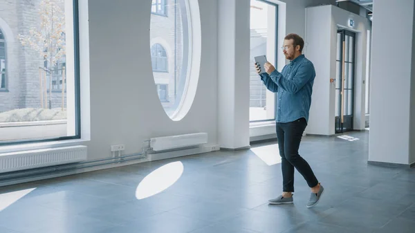 Ung Hipster Man i Jeans Shirt Stående i Tom Office och kartlägga den med en Augmented Reality Software på en surfplatta. Solljus lyser genom stora fönster. — Stockfoto