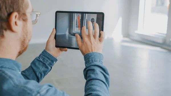 Young Hipster Man in Glasses Debout dans le bureau vide et cartographiez-le avec un logiciel de réalité augmentée sur une tablette. Écran avec application caméra. — Photo