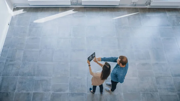 Young Hipster Man and Female Sta in een leeg wit kantoor en breng het in kaart met een Augmented Reality Software op een tablet. Zonlicht schijnt door grote ramen. — Stockfoto